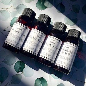 May include: Four small glass bottles with black caps filled with dark red liquid. Each bottle has a white label with black text that reads "Premium Fragrance Oil 50mls" and a different scent: "French Pear", "Caramel Vanilla", "Coconut & Lime", and "Raspberry & Vanilla".