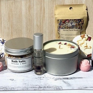 Op de afbeelding: Een spa-cadeauset met een verscheidenheid aan producten, waaronder badzout, een kaars, een kamerverspray, een badbom en een zeep. De producten zijn allemaal in witte en zilveren verpakkingen met bloemmotieven. De set is perfect voor ontspanning en verwennen.