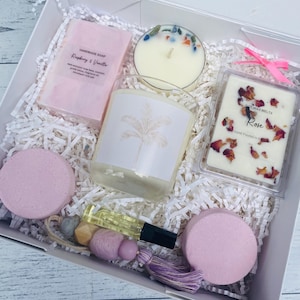 May include: A white gift box filled with pink and white bath products, including soap, bath bombs, and a candle. The box also includes a soy wax melt with the text "Soy Wax Melts Rose Hand Poured x 4 oz".