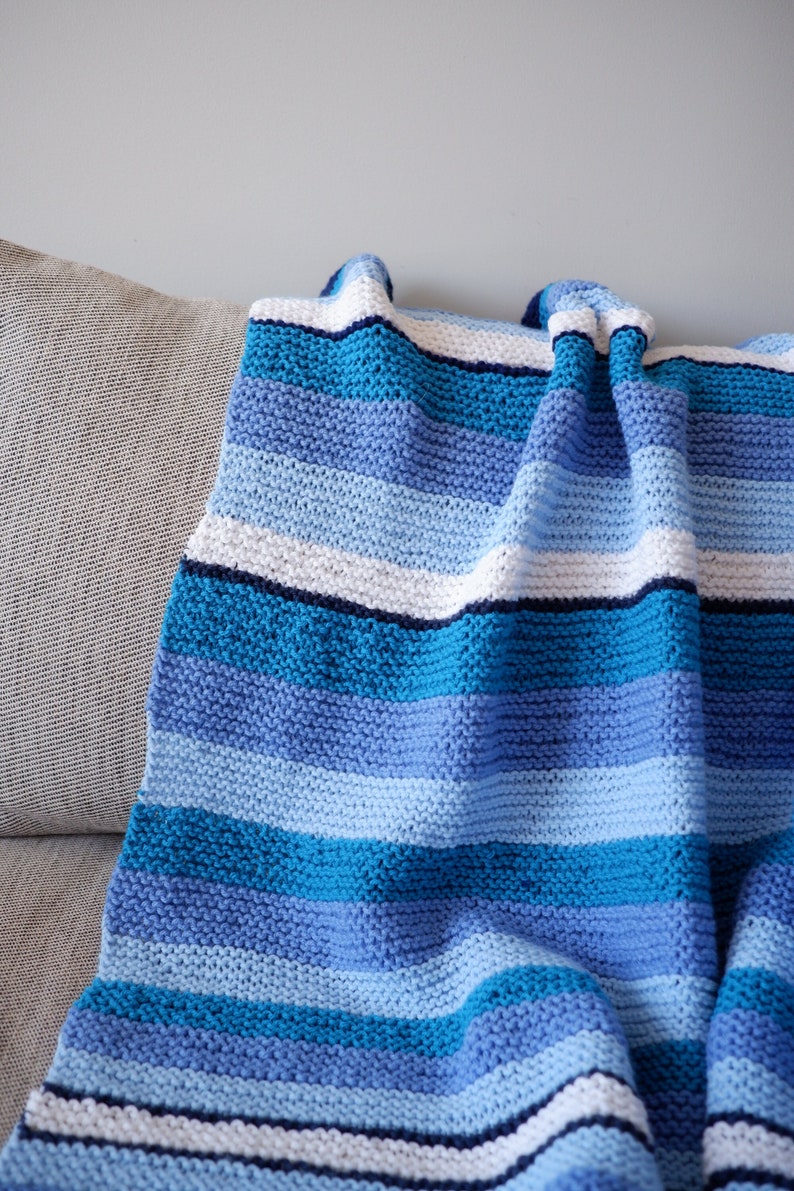 May include: A striped knitted throw blanket in shades of blue, white, and navy. The blanket is folded and draped over a couch.