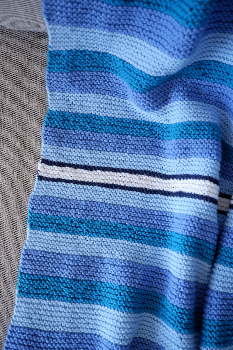 May include: A blue and white striped knitted blanket with a textured pattern. The blanket is folded and draped over a couch.