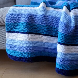 May include: A blue and white striped knitted throw blanket draped over a couch.