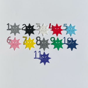 May include: Eleven colorful star-shaped tokens with a black and white angry face design. Each token is numbered 1 through 11.