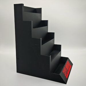 May include: Black, stepped display stand with five tiers. The stand has a rectangular base with the words "SUPER NINTENDO" in red. The stand is designed to showcase collectibles.