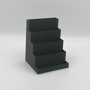 May include: A black plastic desktop organizer with four tiers. The organizer is designed to hold pens, pencils, and other office supplies.