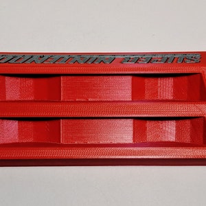 May include: A red 3D printed storage organizer with two compartments. The organizer has the text "SUPER MARIO" printed on the top.