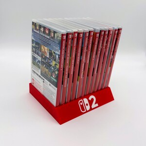 Pu&ograve; includere: Un supporto rosso per giochi Nintendo Switch con logo bianco, contenente diverse cartucce di gioco. Le custodie dei giochi sono rosse, con titoli visibili come "Xenoblade Chronicles 2" e "The Legend of Zelda: Tears of the Kingdom".