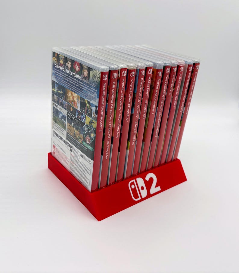 Pu&ograve; includere: Un supporto rosso per giochi Nintendo Switch con logo bianco, contenente diverse cartucce di gioco. Le custodie dei giochi sono rosse, con titoli visibili come "Xenoblade Chronicles 2" e "The Legend of Zelda: Tears of the Kingdom".