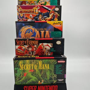 May include: Stacked vintage Super Nintendo game boxes, including "Mario is Missing!" and "Secret of Mana." The boxes feature colorful artwork and game titles. The display stand reads "Super Nintendo Entertainment System."
