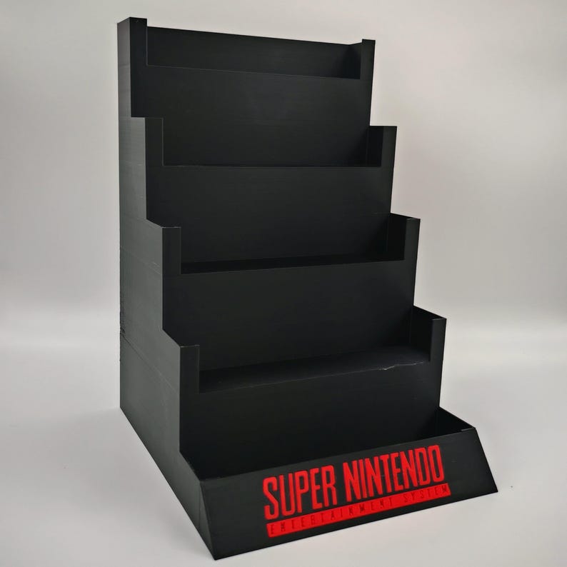 May include: Black, tiered display stand with five shelves. The stand has a stepped design and features the text "SUPER NINTENDO" in red on the front. Ideal for showcasing collectibles or merchandise.