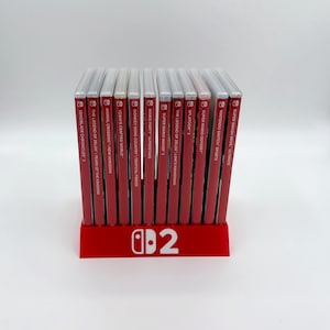 May include: A red Nintendo Switch game holder with the Nintendo Switch logo and the number 2. The holder displays several game cases, including "The Legend of Zelda: Tears of the Kingdom" and "Super Smash Bros. Ultimate."