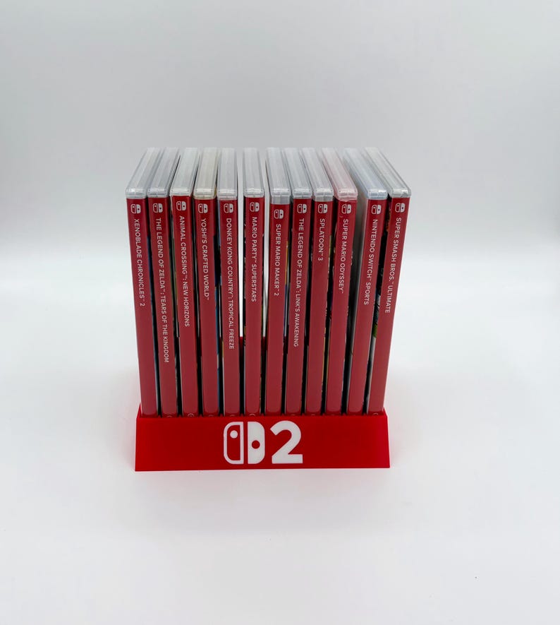 Pu&ograve; includere: Un supporto rosso per giochi Nintendo Switch, con il logo Nintendo Switch e il numero 2. Il supporto mostra diverse custodie di giochi, tra cui "The Legend of Zelda: Tears of the Kingdom" e "Super Smash Bros. Ultimate."