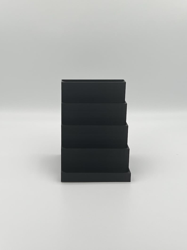 May include: Black plastic desktop organizer with five tiers for storing office supplies.