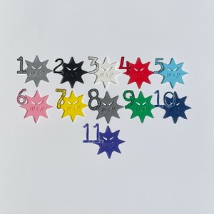 May include: Eleven colorful star-shaped tokens with a black and white angry face design. Each token is numbered 1 through 11.