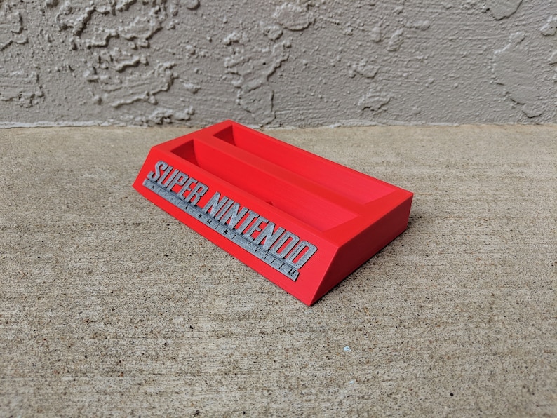 May include: Red plastic Super Nintendo game cartridge holder with two slots. The holder has the Super Nintendo Entertainment System logo on the front.