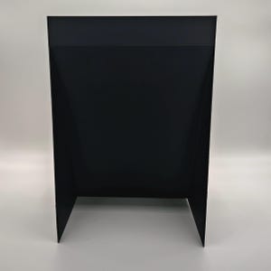 May include: A black, rectangular display stand with a folded design. The stand has a solid black color and is made of a rigid material. The stand has two angled legs for support and a flat top surface.