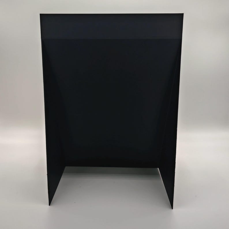 May include: A black, rectangular display stand with a folded design. The stand has a solid black color and is made of a rigid material. The stand has two angled legs for support and a flat top surface.