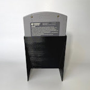 Puede incluir: Soporte de pl&aacute;stico negro para un cartucho de juego de Nintendo 64. El soporte est&aacute; dise&ntilde;ado para mantener el cartucho en posici&oacute;n vertical.