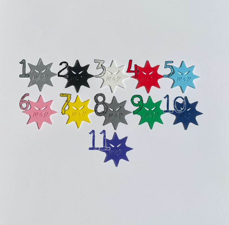 May include: Eleven colorful star-shaped dice with black angry faces and numbers 1 through 11. The dice are arranged in a semi-circle on a white background.