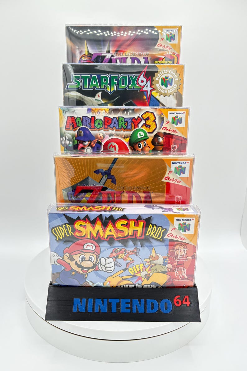 May include: A stack of five Nintendo 64 video game boxes, including "Super Smash Bros" and "Mario Party 3." The boxes are in clear plastic cases and sit on a black base that reads "Nintendo 64."