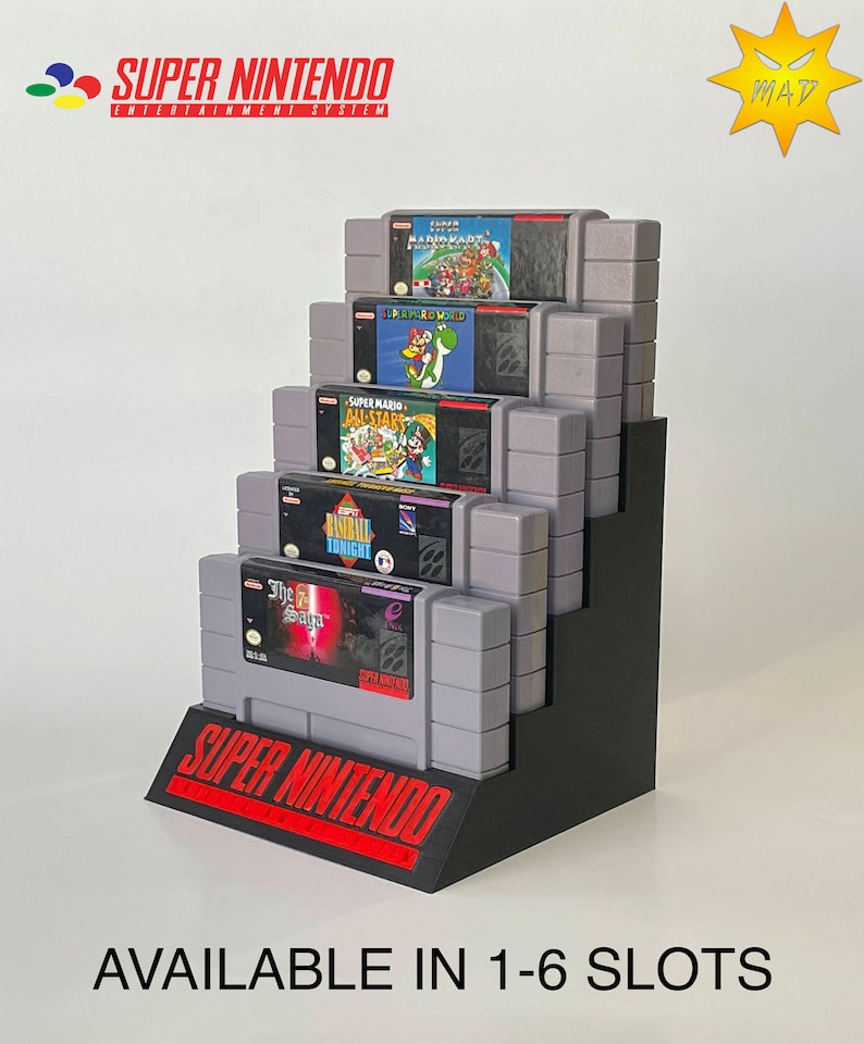Puede incluir: Un expositor negro para cartuchos de juegos Super Nintendo Entertainment System con seis ranuras. El expositor est&aacute; lleno de varios cartuchos de juegos Super Nintendo, incluyendo Super Mario World, Super Mario All-Stars y Baseball Tonight. El expositor est&aacute; etiquetado como "SUPER NINTENDO" y "AVAILABLE IN 1-6 SLOTS".