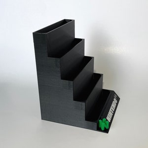 Puede incluir: Organizador de cartuchos de juegos de Nintendo 64 de pl&aacute;stico negro con cinco ranuras. El organizador tiene un logotipo de Nintendo verde en la parte delantera.