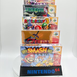 May include: A stack of Nintendo 64 game boxes, including "Super Smash Bros," "Mario Party 3," and "Star Fox 64." The boxes are in protective cases and displayed on a black stand with "Nintendo 64" printed on it.