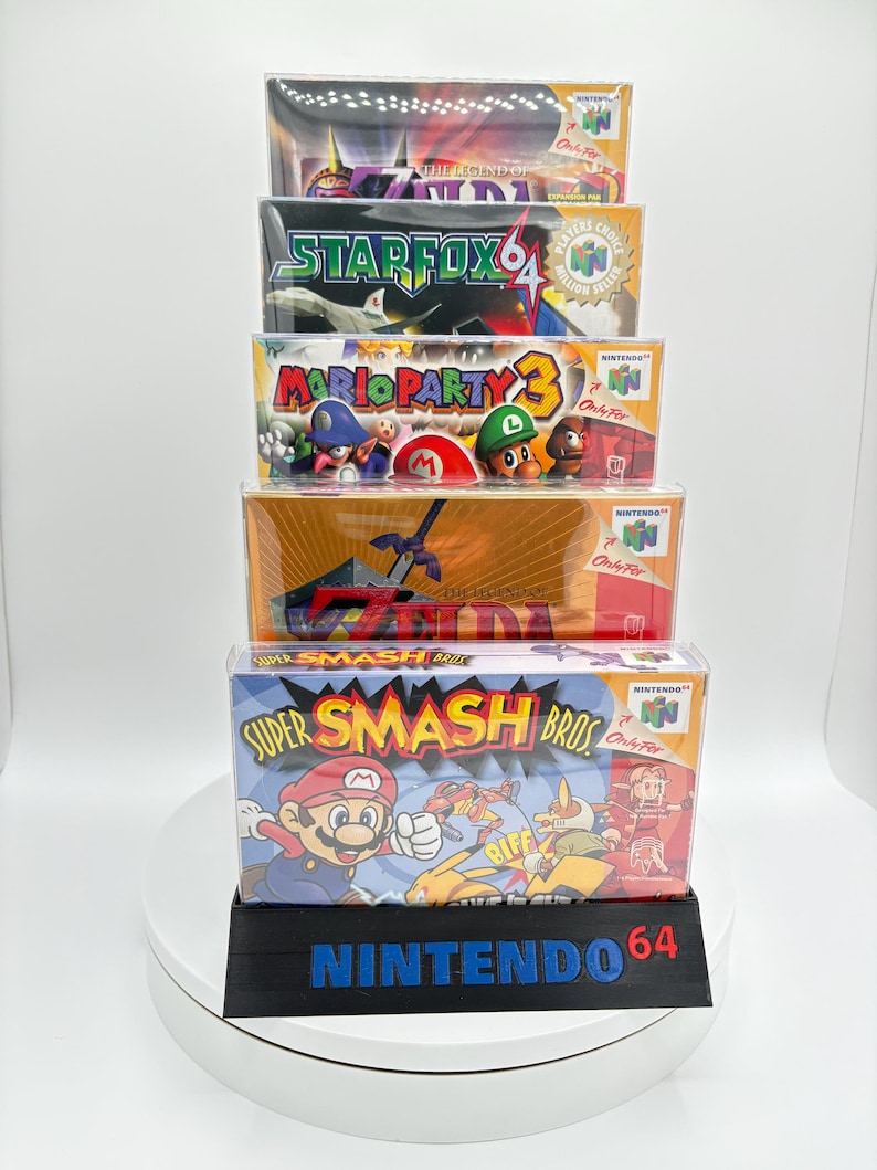 May include: A stack of Nintendo 64 game boxes, including "Super Smash Bros," "Mario Party 3," and "Star Fox 64." The boxes are in protective cases and displayed on a black stand with "Nintendo 64" printed on it.
