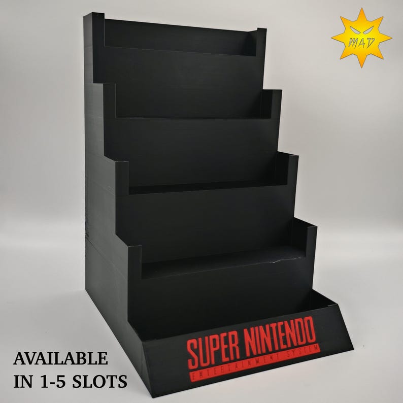 May include: Black tiered display stand with the text "SUPER NINTENDO ENTERTAINMENT SYSTEM" in red. The stand has multiple shelves and the text "AVAILABLE IN 1-5 SLOTS" in black.