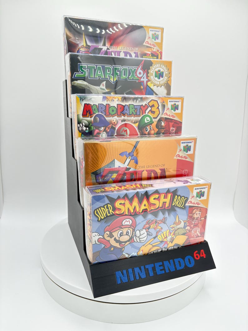 May include: A black display stand holding five Nintendo 64 video game boxes. The games include "Super Smash Bros," "The Legend of Zelda," "Mario Party 3," and "Star Fox 64." The stand has the Nintendo 64 logo in blue.