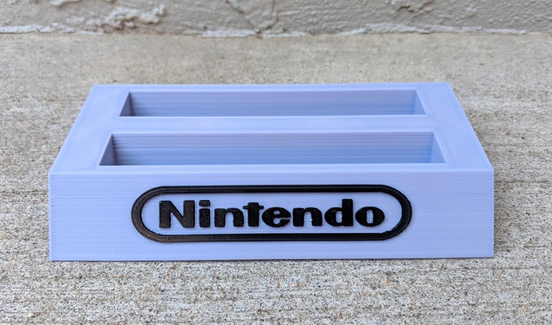 May include: A light purple plastic game cartridge holder with two slots and the Nintendo logo on the front.