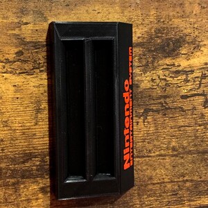 May include: Black plastic game cartridge holder with two slots and the text "Nintendo Entertainment System" in red.