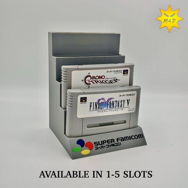 Puede incluir: Un expositor gris para cartuchos de Super Famicom que contiene dos cartuchos de juego. Los cartuchos est&aacute;n etiquetados como "Chrono Trigger" y "Final Fantasy V". El expositor tiene el texto "Super Famicom" y "Disponible en 1-5 ranuras".