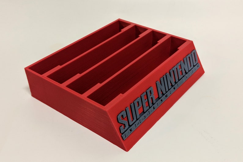 May include: Red plastic game cartridge holder with four slots and the text "SUPER NINTENDO" on the side.
