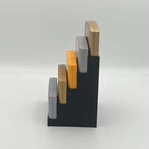 May include: A black plastic stand with five slots for holding game cartridges. The cartridges are in various colors, including gold, silver, and orange.