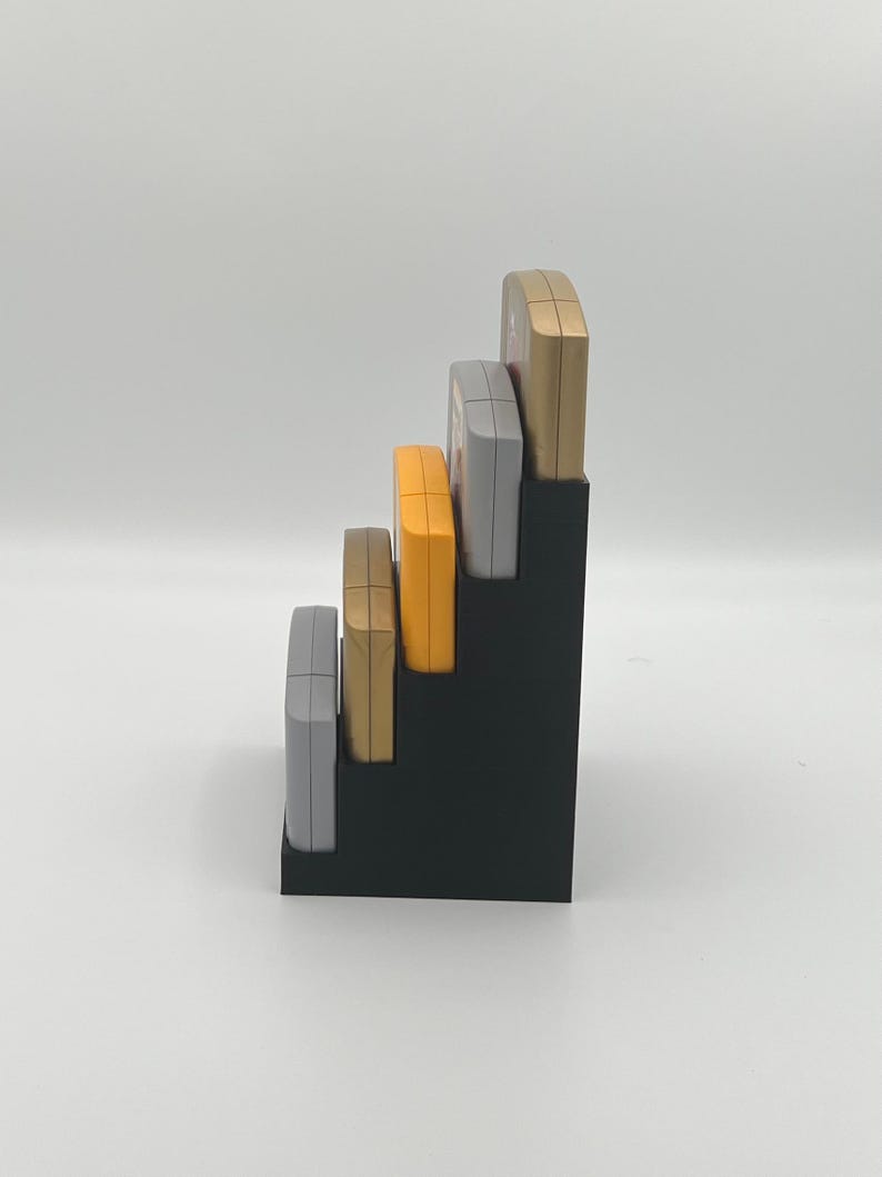 May include: A black plastic stand with five slots for holding game cartridges. The cartridges are in various colors, including gold, silver, and orange.