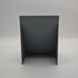 Puede incluir: Un expositor rectangular gris oscuro con un dise&ntilde;o recortado. El expositor est&aacute; hecho de un material s&oacute;lido y tiene una est&eacute;tica simple y moderna. El expositor est&aacute; dise&ntilde;ado para sostener o exhibir art&iacute;culos.