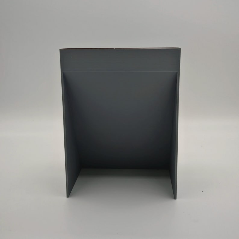 Puede incluir: Un expositor rectangular gris oscuro con un dise&ntilde;o recortado. El expositor est&aacute; hecho de un material s&oacute;lido y tiene una est&eacute;tica simple y moderna. El expositor est&aacute; dise&ntilde;ado para sostener o exhibir art&iacute;culos.