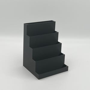 May include: A black plastic tiered desktop organizer with four compartments. The organizer is designed to hold business cards, pens, or other small office supplies.