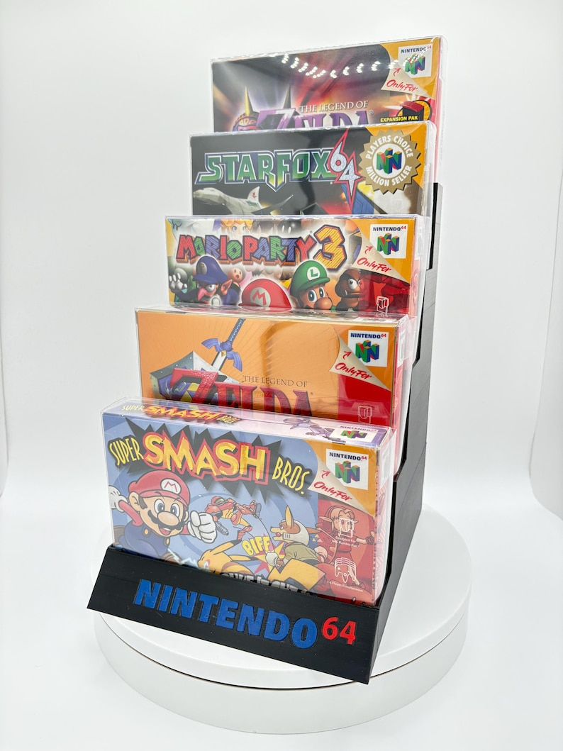 May include: A black display stand holding five Nintendo 64 video game boxes. The boxes feature game titles like "Super Smash Bros" and "Mario Party 3." The stand has the words "NINTENDO 64" in blue and red.
