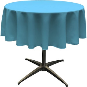 May include: A round table with a light blue tablecloth. The tablecloth drapes over the edge of the table. The table has a dark metal base with a star-shaped design.