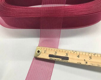 May include: A roll of burgundy mesh ribbon with a ruler measuring its width. The ribbon is a deep red-purple color and has a fine, open weave. The ruler shows the ribbon is approximately 2 inches wide.