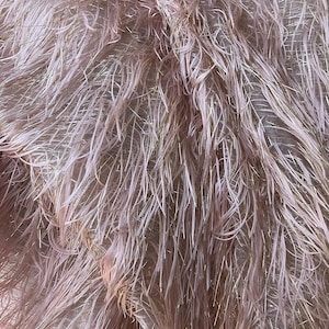 May include: Close-up of a fluffy, textured fabric in a soft pink hue. The material is densely packed with long, delicate strands, interspersed with strands of gold. The overall effect is a luxurious, feathery appearance.