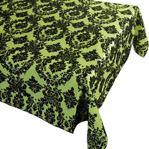 May include: A rectangular tablecloth featuring a vibrant lime green base color with a repeating black damask pattern. The fabric drapes over the corner of a surface, displaying the intricate, symmetrical floral and scrollwork design clearly.