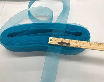 May include: A roll of turquoise tulle ribbon with a ruler showing the width. The ribbon is a light, sheer material, ideal for crafts and decorations. The ruler shows the ribbon is approximately 2 inches wide.