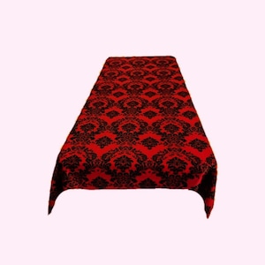 May include: A rectangular table runner featuring a vibrant red background with a repeating black damask pattern. The fabric displays a symmetrical, ornate floral motif that covers the entire surface, creating a bold contrast between the two colors.