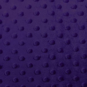 May include: Close-up of a deep purple fabric with a textured, raised dot pattern. The plush material has a soft, velvety appearance. The design features evenly spaced, rounded bumps across the surface, creating a tactile and visually appealing texture.