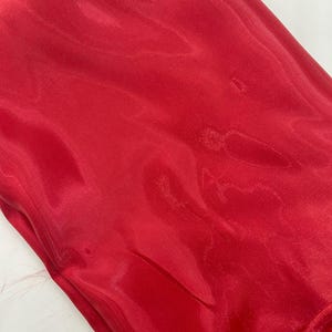 May include: A vibrant red fabric with a glossy sheen. The material appears to be lightweight and flowing, with subtle folds and highlights. The fabric's color is a rich, solid red, suggesting it could be used for apparel or decorative purposes.
