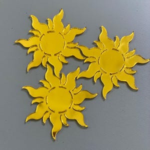 May include: Three gold mirror sun-shaped ornaments with a textured surface. Each ornament has a circular center and 12 points radiating outward.