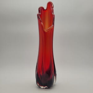 May include: A tall, red glass vase with a flared top. The vase has a slender, elongated shape, with a gradient of colour from deep red at the base to a lighter orange at the top. The vase is approximately 30 cm tall.